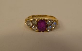 An 18ct gold ring, set with a central pink/red stone, flanked by six diamonds