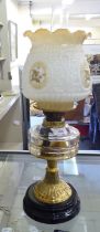 A late Victorian brass oil lamp with a moulded glass reservoir, on a pedestal base and black ceramic
