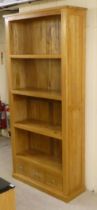 A modern light oak and plywood backed, open front, four tier bookcase with three drawers, on a