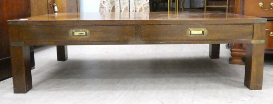 A modern mahogany finished coffee table with two drawers and brass capped corners, raised on block
