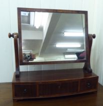 An early 19thC mahogany toilet mirror, the crossbanded plate pivoting on scrolled horns and a