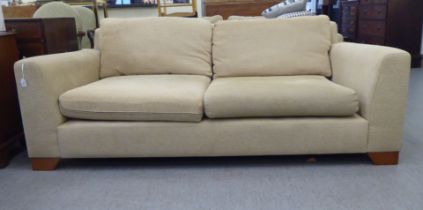 A modern two person settee, upholstered in oatmeal coloured fabric with a level back and arms,