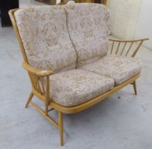 An Ercol blonde beech and elm framed settee with a spindled, level back and open arms, raised on