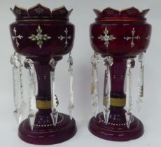 A pair of late 19thC ruby coloured glass lustre vases with overpainted, enamelled ornament, the