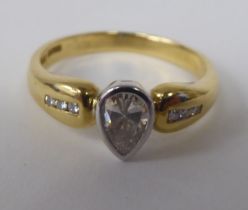 A gold coloured metal ring, set with a single stone, pear shaped diamond, between diamond shoulders