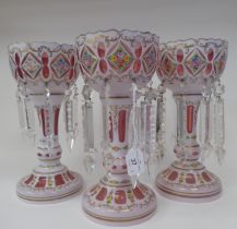 A set of three late 19thC Continental cranberry coloured glass lustre vases with overlaid white