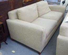 A modern two person settee, upholstered in oatmeal coloured fabric with a level back and arms,