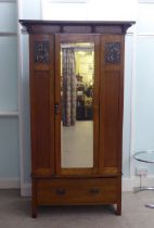 An Arts & Crafts period oak wardrobe with a mirrored door and pressed brass effect panels, over a