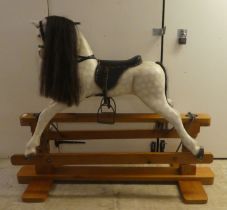 A modern hardwood dapple grey painted rocking horse with a leatherette saddle, raised on a pillar