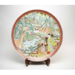 A Japanese circular charger, decorated with figures in a mountainous village landscape.