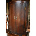 An antique crossbanded oak bow front hanging corner cupboard