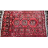 An Afghan red ground rug, the triple octagonal lozenge design within stylised floral borders, 118 cm