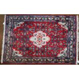 Small Persian red ground rug, stylised floral design around central cream medallion, blue