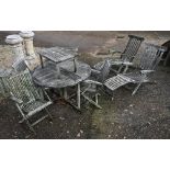 A heavily weathered teak circular garden table and set of four armchairs to/w a pair of teak steamer