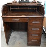 A small early 20th century oak roll-top desk, the pull-down tambour panel enclosing fitted