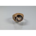 A 1970s style cocktail ring set with oval smokey quartz, claw set above high carved shoulders, 9ct