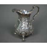 A George II silver pear-shaped cream jug with scroll handle and trefoil pad feet, richly embossed