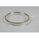 A narrow oval half hinged bangle fitted with safety chain, unmarked and untested, approx 4.9g