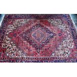 A Persian Heriz carpet of traditional design, the red ground centred by a medallion in reds and