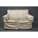 A traditional two-seat sofa with gold silk loose covers over patterned undercloth, raised on hip