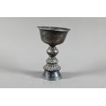 A 19th century Tibetan silver yak butter lamp, the bowl with everted rim richly engraved with leiwen