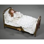 A French automaton bisque-head Armand Marseille girl doll, in a brass bed, 38 cm wide overall; she