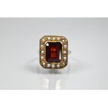 A yellow metal ring of rectangular design featuring emerald-cut red stone, probably garnet,