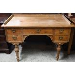 An old stripped pine five drawer desk and 3/4 galleried top, raised on turned legs (one leg