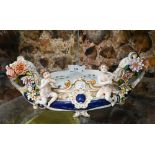 A Continental porcelain oval flower trough mounted with two musical putti and encrusted with
