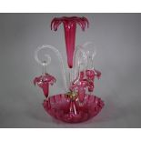 A Victorian cranberry glass epergne with central foliate flute flanked by three baskets on curling