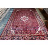 An old Persian Hamadan carpet, the red ground with repeating stylised floral design centred by a