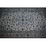 A Persian Kashan carpet, the pale camek ground with floral vine design within blue borders, 355 cm x