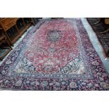 A large Persian Kashan red ground carpet, with flowering vine design centred by blue ground