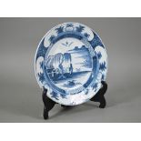 A Delft blue and white plate, painted with chinoiserie coastal landscape within foliate reserves