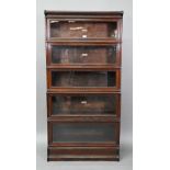 A dark oak five section Globe Wernicke library bookcase, with glazed-in hinge-over doors, on a
