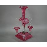 A Victorian cranberry glass epergne with central flute vase flanked by two floral flutes and two