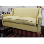 A two-seater Kersey sofa with woven lime fabric and brown piping, light oak tapering square supports