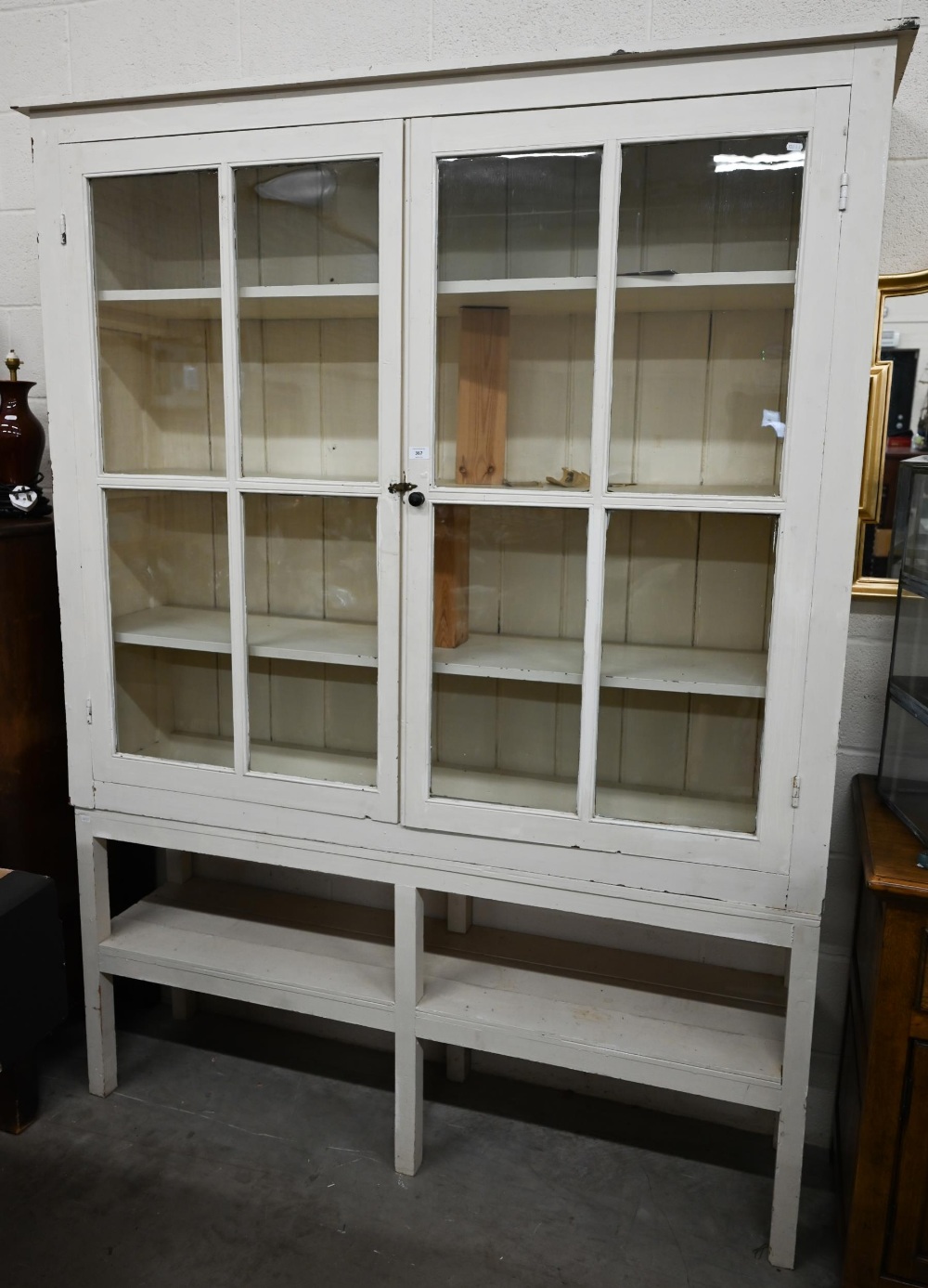 A large cream painted pine bookcase with glazed doors enclosing three shelves with open shelf below,