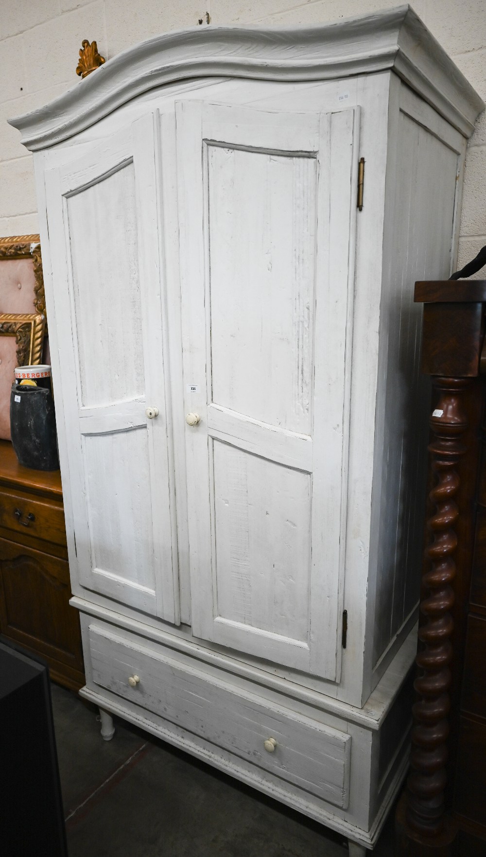 A cream painted pine armoire wardrobe with panelled doors and single drawer (in two sections), by