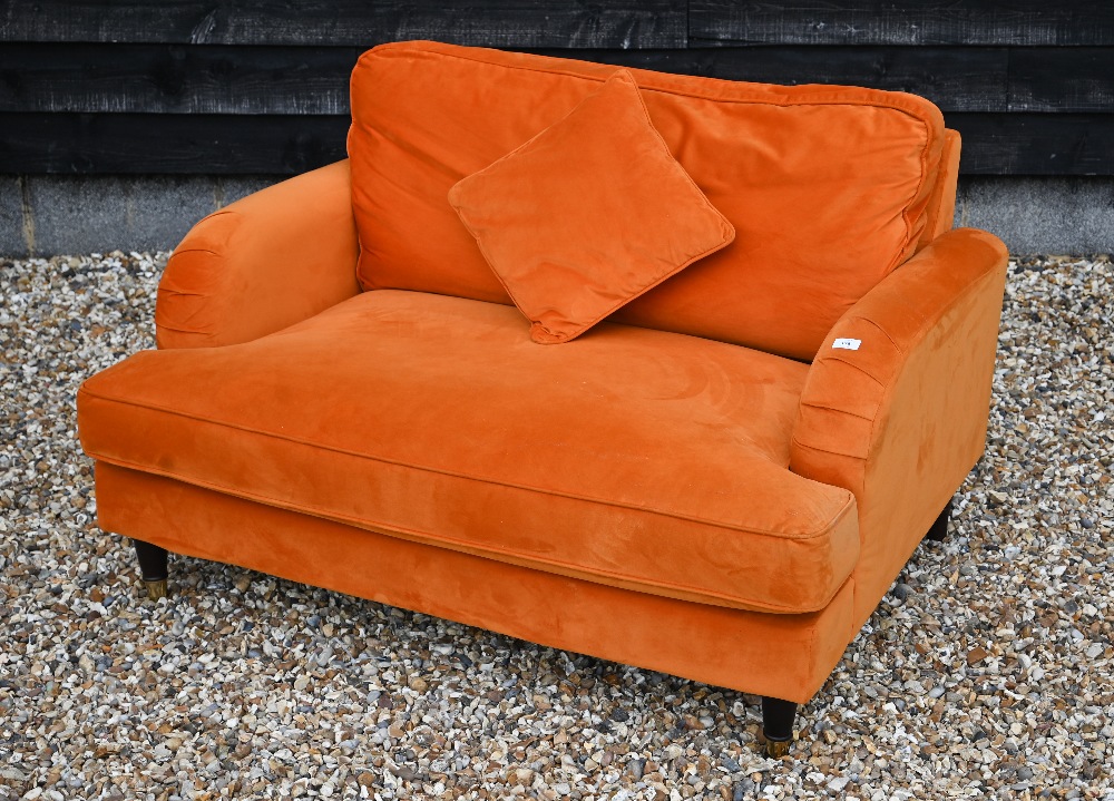 A contemporary plush burnt orange upholstered 'love chair', raised on turned front legs to brass