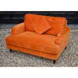 A contemporary plush burnt orange upholstered 'love chair', raised on turned front legs to brass