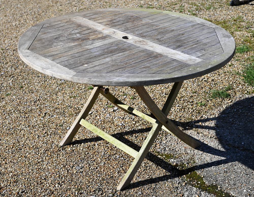 A weathered teak circular garden dining table on folding frame, 120 cm diam x 72 cm high
