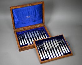 An Edwardian oak-cased set of twelve each silver dessert knives and forks with engraved blades and