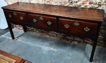 An 18th century oak low dresser, the wide single plank top over three drawers within a shaped apron,