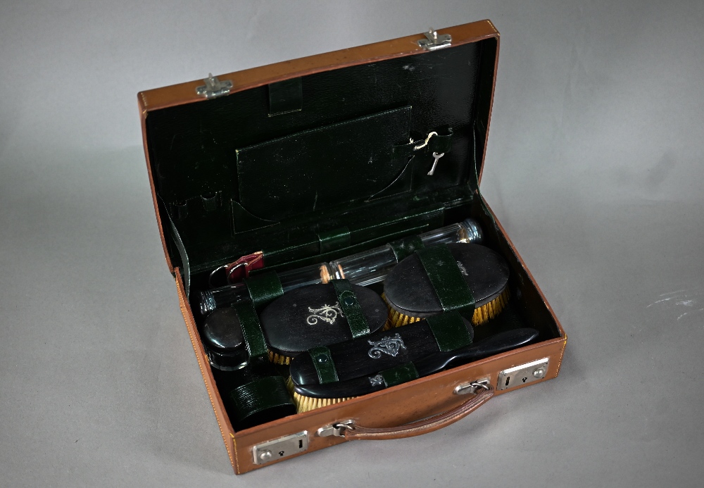 A leather toiletry case, the green Morocco interior fitted with ebony brushes with unmarked silver