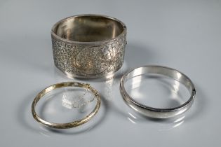 A wide white metal oval half-hinged bangle with engraved floral decoration to front, stamped '
