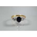 A three-stone sapphire and diamond ring, the central oval blue sapphire with a circular diamond to