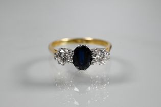 A three-stone sapphire and diamond ring, the central oval blue sapphire with a circular diamond to