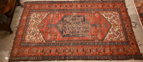 A worn Caucasian red ground rug with navy medallion and floral motifs,  190 x 115 cm