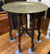 An old Middle Eastern engraved brass tray top table, on folding hardwood base, 58 cm dia. x 62 cm h